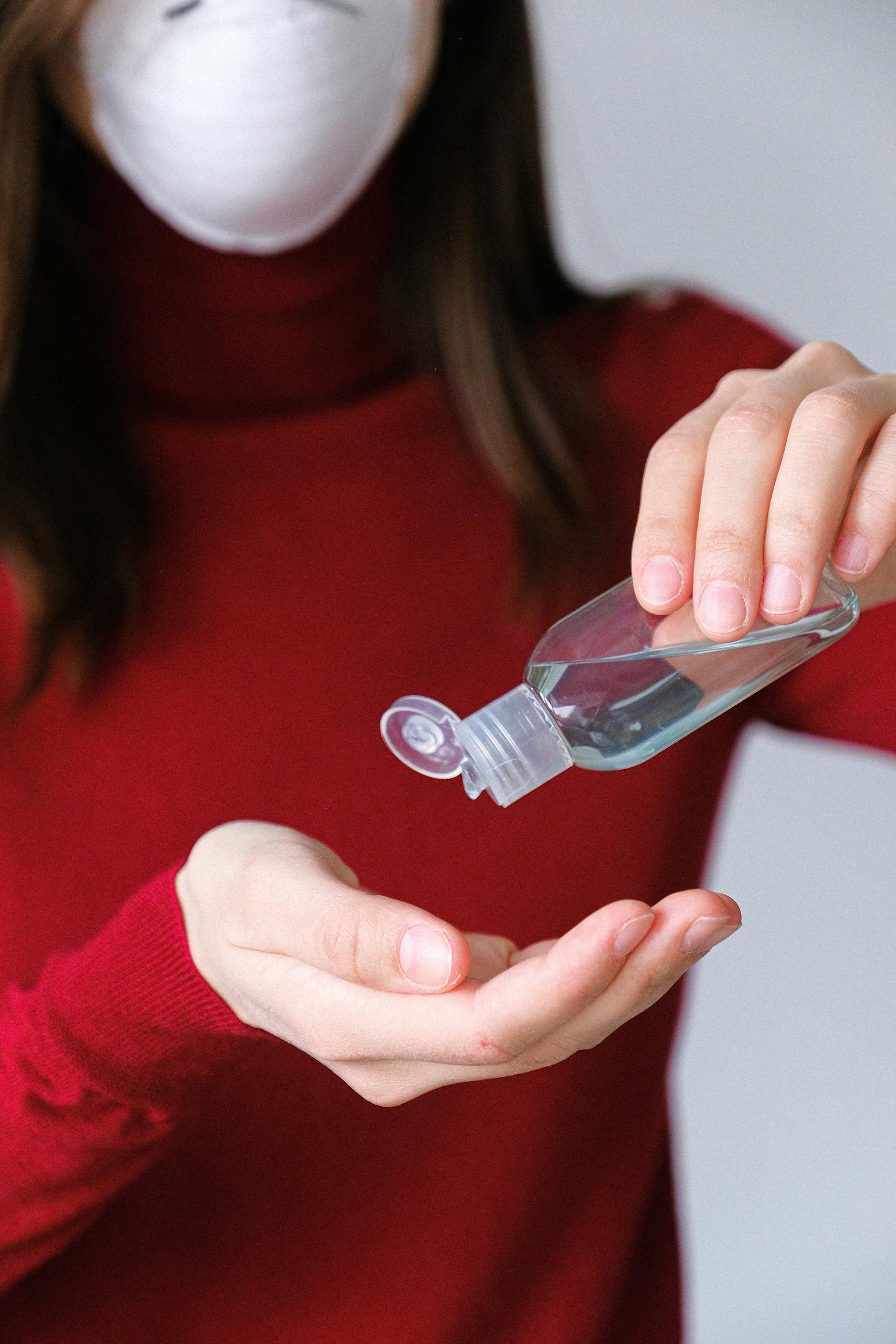 A woman in a red sweater applies hand sanitizer indoors for hygiene and prevention.